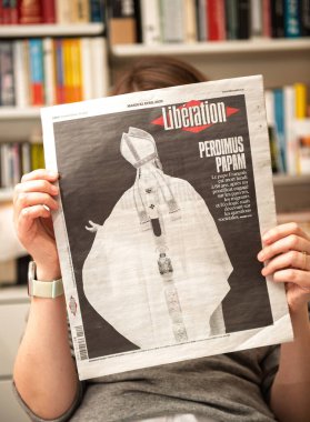 Paris, Fransa - 22 Nisan 2025: Bir kadın, Liberasyon gazetesinin ön sayfasını rahat bir iç mekan ortamında okuyor ve Papa Francis 'in Latince Perdimus Papam tabiriyle ölümünün başlığını atıyor.