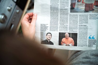 Paris, Fransa - 22 Nisan 2025: Bir kadın Papa Francis 'in muhtemel halefleri hakkında bir Fransız gazetesi makalesi okuyor, Kardinaller Tagle ve Zuppi' nin portrelerini ayrıntılı yorum ve analizlerle gösteriyor.