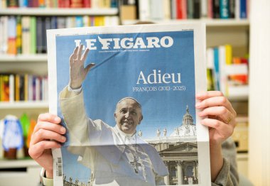 Paris, Fransa - 22 Nisan 2025: Konforlu bir oturma odasında oturan bir kadın, Papa Francis 'in veda manşeti ve el salladığı görüntüsünü gösteren bir Le Figaro gazetesini elinde tutuyor.