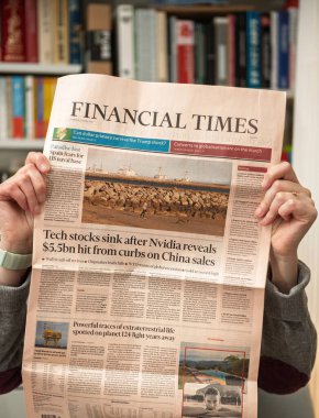 Paris, Fransa - 22 Nisan 2025: Financial Times gazetesinde Nvidia 'nın pazar düşüşü ve ABD-Çin gerginlikleri hakkında ön sayfa manşeti bulunan bir kişi, arka planda kitaplıklarla kapalı mekanlarda gösteriliyor