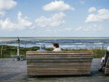 Egmond aan Zee, Hollanda - 25 Ağustos 2024: İki kişi, rüzgârlı Kuzey Denizi 'ne bakan ahşap bir bankta oturuyor..