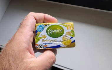 Paris, Fransa - 28 Ağustos 2024: Bir el küçük bir paket Campina Botergoud tuzsuz tereyağını, renkli ambalaj ve besin etiketi üzerine ayrıntılı bir şekilde odaklanmış, kapalı bir arka planda tutuyor..