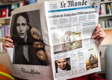 Paris, Fransa - 13 Kasım 2024: Bir kişi Le Monde gazetesinde Trump 'ın iklim haberleri ve mücevher reklamının yanında kitap ve mobilyaların yanında otururken zafer başlığını okudu