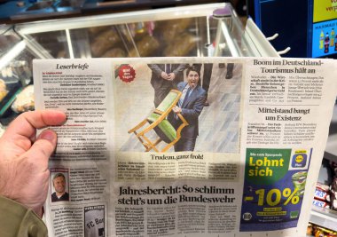 Paris, Fransa - 12 Mart 2025: Justin Trudeau 'nun turizm, Bundeswehr ve ekonomik kaygıları tartışan manşetlerle çevrili, ahşap bir sandalyeyi kaldırırken gülümsediği bir ön sayfa fotoğrafı içeren bir Alman gazetesini tutan el..