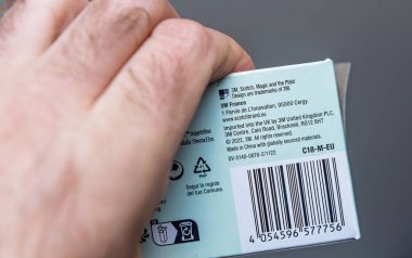 Paris, Fransa - 18 Nisan 2025: Açık mavi bir 3M ürün kutusunu elinde tutan ve imalatçının adresini gösteren barkod ve simgeleri yumuşak gün ışığında nötr bir arkaplana karşı geri dönüşüm simgelerini gösteren yakın plan