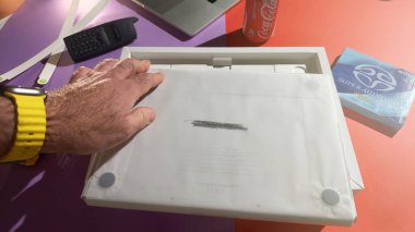 Paris, Fransa - 4 Nisan 2025: Sarı saat takan bir el yeni bir MacBook Pro M4 Max 'i kutusundan kaldırır, logosu görünür bir şekilde korunmak için yazılır, renkli ve modern eşyalarla çevrili bir masa üzerinde..