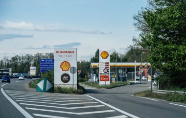 Fransa, Fransa - 20 Nisan 2025: Açık gökyüzü altında karşılama işaretleri ve yol işaretleriyle Colmar ve Selestat yakınlarındaki bir Fransız otoyolu çıkışında görünür tabela ve yakıt fiyatlarıyla deniz kabuğu akaryakıt istasyonu kuruldu