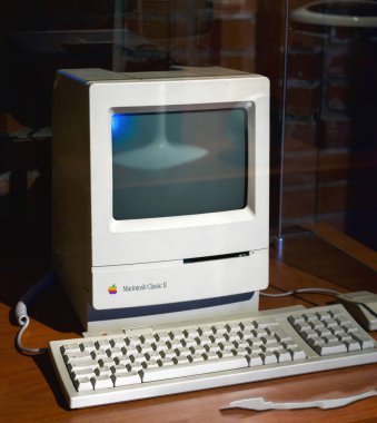 Paris, Fransa - 20 Nisan 2025: Entegre CRT ekranlı, bozuk beyaz çantalı ve eşleşen klavyeli klasik Apple Macintosh Classic II kişisel bilgisayarı, sergi ışıkları altında ahşap bir masanın üzerine yerleştirildi.