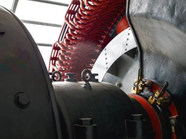Ağır siyah metal konutları, kırmızı bakır bobinleri ve pirinç konnektörleri gösteren antika bir elektrik jeneratörünün yakın çekimi.