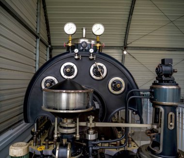 Paris, Fransa - 20 Nisan 2025: İki analog basınç göstergesinin, simetrik döngü bileşenlerinin ve kavisli bir siyah metal kaplama içinde bulunan mekanik parçaların yer aldığı büyük bir vintage endüstriyel makinenin ön görünümü
