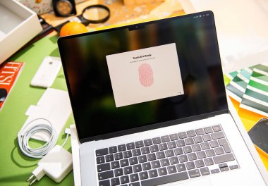 Paris, Fransa - 13 Mart 2025: MacBook Pro M4 Max Dokunmatik Kimlik kurulumu sırasında renkli masada, parmak izi doğrulama ekranını cihazın etrafına yerleştirilmiş aksesuarlar, şarj aletleri ve teknolojik aletlerle gösteriyor