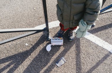 Strasbourg, Fransa - Ocak 12025: Kışın giydiği küçük bir çocuk, kullanılmış bir havai fişek kutusunun yanında asfalt üzerinde duruyor ve yeni yıl kutlamalarının soğuk gün ışığında sona ermesini yansıtıyor.