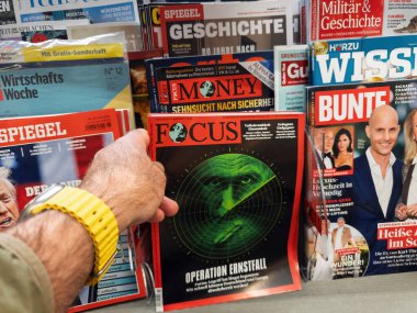 Frankfurt, Almanya - 9 Nisan 2025: Meşgul bir büfede diğer Alman yayınları tarafından çevrelenmiş, Ernstfall Operasyonu başlıklı yeşil radar temalı bir Focus dergisini elinde tutan kişi