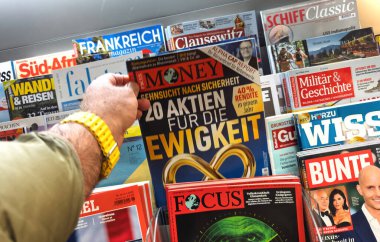 Frankfurt, Almanya - 9 Nisan 2025: Ekonomi ve yaşam tarzı temalı yoğun bir gazete bayiinde çeşitli Alman yayınları arasında yatırım manşetleri bulunan Focus Money dergisini alan kişi