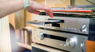 PAris, Fransa - 22 Nisan 2025: Bir el, Onkyo P-3000R ön amplifikatörünün üzerinde yer alan gümüş bir Onkyo oynatıcısının tepsisine CD ve vinil plakların üst üste istiflendiği bir CD yükler