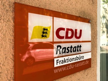 Rastatt, Almanya - Mayıs 12025: Devlet amblemli turuncu CDU Rastatt FraktionsbUro tabelası Freiburg 'da park halindeki bir arabayı ve parlak yüzey çevresini yansıtan dokulu bir dış duvara asıldı