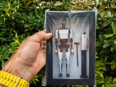 Frankfurt, Almanya - 5 Mayıs 2025: Nadir bulunan Tesla Bot koleksiyoncusu figürü, yeşil yapraklı bir arkaplana karşı sergilenen modüler robotik bileşenleri içeren plastik ambalajda tutulup mühürlendi