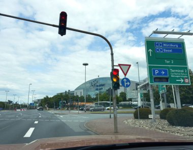 Frankfurt, Almanya - 7 Mayıs 2025: Frankfurt Havaalanı 'nın 2 numaralı terminali yakınlarındaki trafik ışıkları ve istikamet işaretleri Wurzburg, Basel ve araba kiralama alanlarının parçalı bulutlu bir gökyüzü altında olduğunu gösteriyor