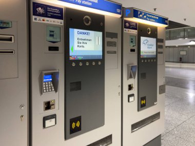 Frankfurt, Almanya - 7 Mayıs 2025: Frankfurt Havalimanı 'ndaki modern otopark ödeme istasyonları çok dilli arayüzleri ve kart ödeme seçeneklerini göstererek, temiz bir terminal bölgesinde parasız işlemleri gösteriyor