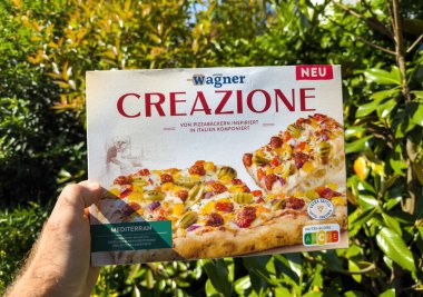 Paris, Fransa - 17 Mayıs 2025: Bir kutu Wagner Creazione Akdeniz pizzası, arka planda parlak yeşil yapraklı, güneşte kızartılmış zeytin ve kırmızı pesto bulunmakta.