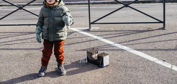 Strasbourg, Fransa - Ocak 12025: Kışlık ceketli ve botlu genç çocuk, yılbaşı kutlamalarından sonra harcanan havai fişek bataryalarının yanında asfalt üzerinde duruyor.