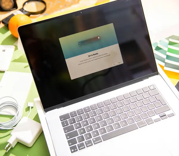Paris, Fransa - Mar 13, 2025: M4 Max çipli MacBook Pro, Siri aktivasyon ekranını, şarj kablosunu, aksesuarları ve etrafındaki renkli elementleri gösteren parlak bir çalışma alanında sergilendi