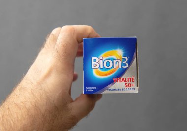 Paris, Fransa - 10 Mart 2025: 50 yaşın üzerinde yetişkinler için tasarlanmış B6, B12, C, D vitaminlerini destekleyen, mavi aminlerde Bion3 Vitalite 50 destek kutusunu tutan bir elin yakın çekimi.