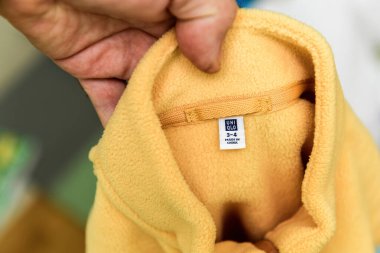 Paris, Fransa - 26 Ekim 2024: Bir el yeni sarı yün bir ceketin yakasını tutuyor, üzerinde UNIQLO 3-4 yazan iç boyut etiketini gösteriyor, genç çocuklar için giysi renklendiriyor.