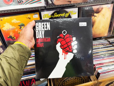 Ulm, Almanya - 6 Mayıs 2025: Bir müzik mağazasında Green Day Amerikan plağı satan bir kişi, ikonik kapak resmi olarak arka planda plakların bulunduğu kırmızı bir kalbi tutan beyaz bir el sergiliyor..
