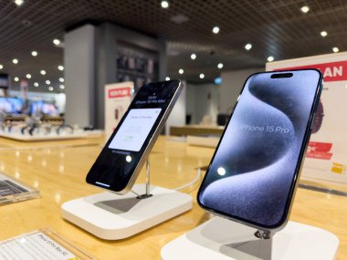Paris, Fransa - 10 Mart 2023: Parlak bir elektronik mağazasında arka planda ahşap tezgahlar, ışıklar ve ürün tabelaları bulunan iki iPhone 15 Pro akıllı telefon sergilenmektedir.