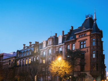 Fransa 'nın Strasbourg kentinde alacakaranlıkta parlak camları ve açık mavi gökyüzü ile gösterişli ön cepheleri ve belirgin bir tareti olan zarif tarihi binalar aydınlatılıyor..