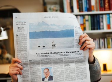 Paris, Fransa - 21 Ocak 2025: OYİ 'nin katı göç planı ve ön sayfasında göl fotoğrafı olan bir gazete okuyan kişi.