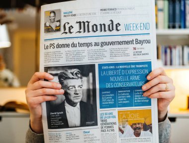 Paris, Fransa - 21 Ocak 2025: Eller, David Lynch 'in monokrom portresini içeren Fransız Le Monde gazetesinin hafta sonu baskısını bulanık bir kitaplıkta siyasi manşetler arasında kavrıyor.