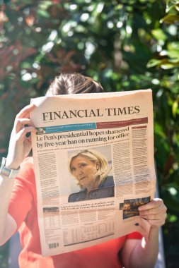 Paris, Fransa - 9 Nisan 2025: Kırmızı tişörtlü bir kişi Financial Times gazetesini açık havada tutuyor, yüzlerini kısmen gizliyor ve başlık Marine Le Pen 'in beş yıllık görev yasağına odaklanıyor.