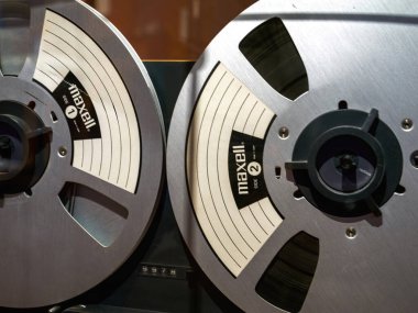 Metalik dokuyu, etiketleri ve manyetik bant sarma mekanizmasını gösteren bir teybe monte edilmiş Maxell 'den makaraya yakın çekim.