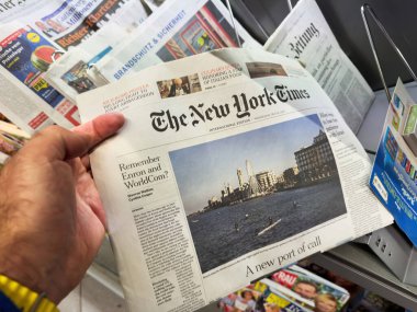 Paris, Fransa - 12 Ocak 2024: Sarı saat takan bir el, New York Times gazetesinin uluslararası baskısında yeni bir liman ve liman manzarası ile ilgili manşetler yer alıyor.