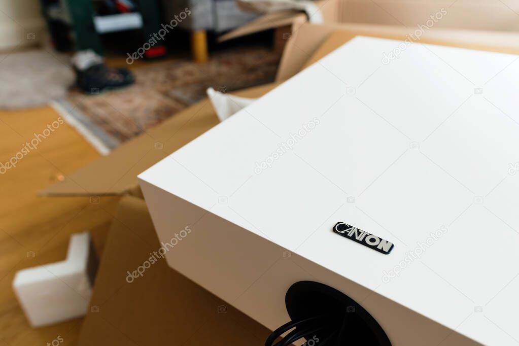 Paris, France - Nov 29, 2024: White Canton subwoofer with a visible logo and front port, placed on a cardboard box with foam packaging nearby, background shows part of a patterned rug and a home interior