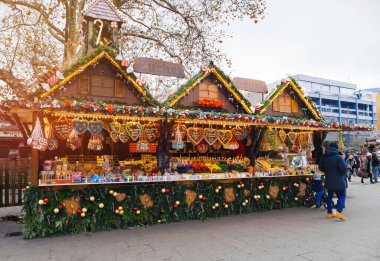 Baden-Baden, Almanya - 1 Aralık 2024: Baden-Baden Noel pazarında çelenk ve peri ışıklarıyla süslenmiş şeker, zencefilli ekmek ve şeker satan renkli bayram standı