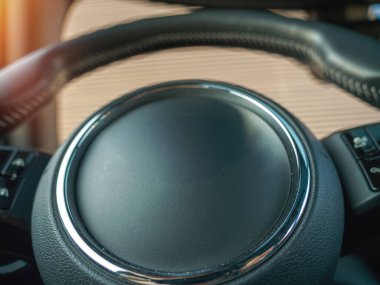 Merkezi rozet alanı kasıtlı olarak boş, kroma halkasıyla çerçevelenmiş ve dokulu kavrama ve kontrol düğmelerinin bir kısmını gösteren jenerik bir direksiyon simidi..