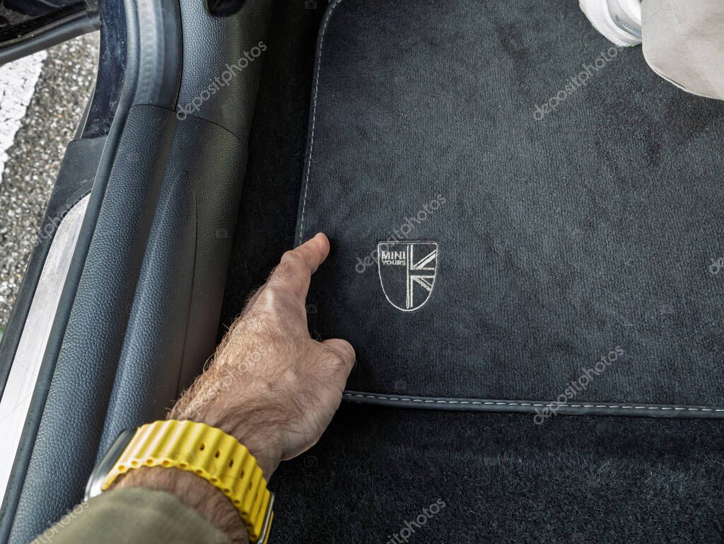 Paris, France - Mar 27, 2025: A hand with a yellow watchband points to the black carpet of a Mini Cooper, highlighting the embroidered MINI Yours logo near the passenger seat footwell area