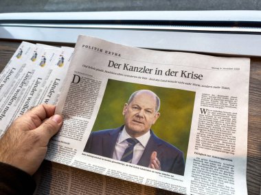 Freiburg, Almanya - 6 Kasım 2023: Olaf Scholz 'un olduğu bir Alman gazetesini kapağında tutmak, krizle ilgili manşet, tahtadan bir masanın üzerine yığılmış kağıtlarla görünür hale getirmek.