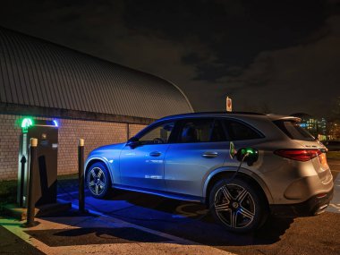 Stuttgart, Almanya - 12 Ekim 2023: Mercedes EQC gece yapay ışıklar altında şarj oluyor, şarj istasyonundan parlak mavi ve yeşil renkler.