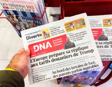 Paris, Fransa - 4 Nisan 2025: Bir kişi Dernieres Nouvelles d Alsace 'i diğer bölgesel Fransız yayınlarıyla çevrili Trump gümrük vergilerine Avrupa tepkisi başlığıyla bir basın büfesinde tutuyor
