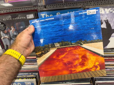 Berlin, Almanya - 3 Temmuz 2025: Red Hot Chili Peppers 'ın sembolik Californication plaklarını arka planda görünen raflar ve diğer albümlerle birlikte Berlin' deki bir plak dükkanında tutan bir el