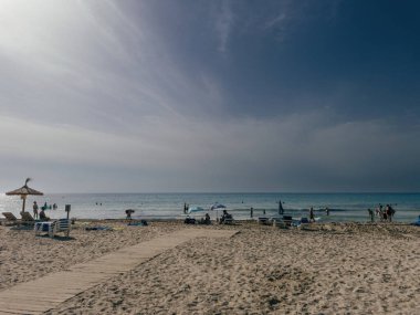 Sa Coma, İspanya - 15 Temmuz 2025: Mallorca 'da güneşlenenleri, güneşlenenleri ve kumsala gidenleri yumuşak bir gökyüzü altında sakin bir denizle gösteren geniş bir manzara