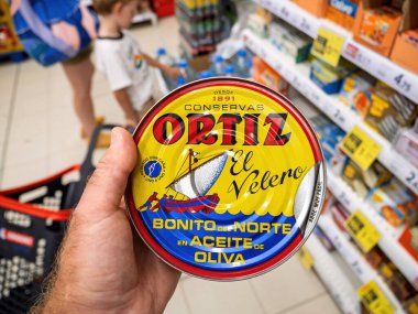 Inca, İspanya - 21 Temmuz 2025: İspanya 'nın Mallorca kentindeki bir süpermarket koridorunda arka planda konserve deniz ürünleri rafları bulunan Bonito del Norte en Aceite de Oliva etiketli sarı bir Ortiz ton balığı konservesini tutan bir el.