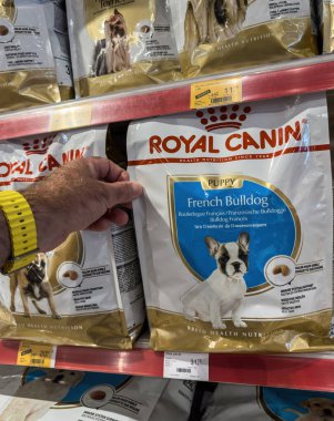 Inca, İspanya - 17 Temmuz 2025: Bir müşteri, Mallorca 'daki bir evcil hayvan dükkanının koridorunda bir çanta Royal Canin Fransız Bulldog Puppy maması tutuyor..