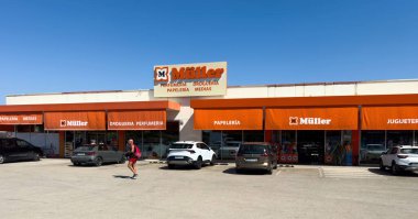 Manacor, İspanya - 21 Temmuz 2025: Mallorca 'daki Muller mağazasının turuncu güneşlikleri ve açık mavi gökyüzünün altında park edilmiş arabalarla dış görünüşü