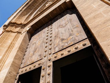 İspanya 'nın Pollenca kentindeki açık mavi gökyüzünün altındaki taş bina cephesinde dekoratif metal çiviler bulunan büyük tarihi ahşap kapının alçak açılı görüntüsü.