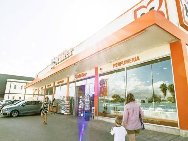 Manacor, İspanya - 21 Temmuz 2025: Bir M ller mağazasının dışı, park halindeki araba ve ziyaretçilerle dolu olan parfüm bölümünü, girişe doğru yürüyen bir kadın ve çocuğu da kapsıyor..